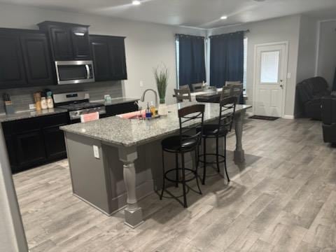 kitchen with appliances with stainless steel finishes, an island with sink, a kitchen bar, and light wood-style floors