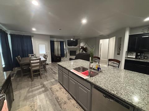 kitchen featuring a fireplace, a sink, open floor plan, light wood-type flooring, and dishwasher