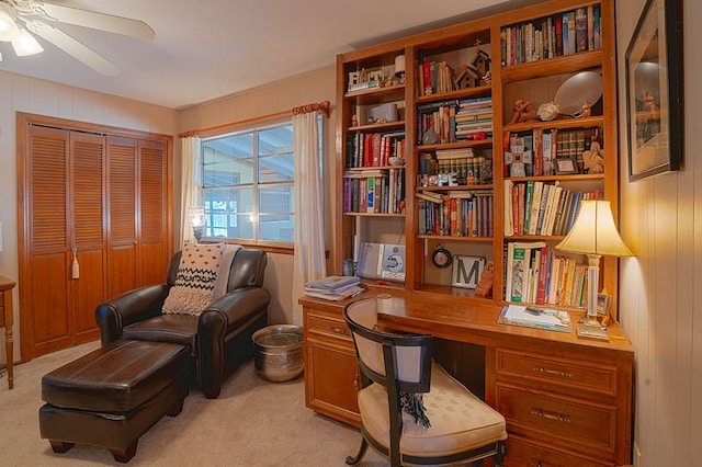 carpeted home office with wooden walls and ceiling fan