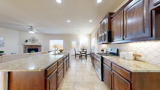 kitchen with ceiling fan, sink, stainless steel appliances, backsplash, and a fireplace