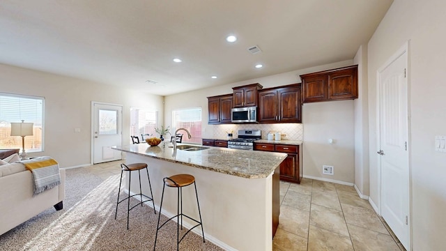 kitchen with a kitchen island with sink, a kitchen breakfast bar, sink, light stone countertops, and stainless steel appliances