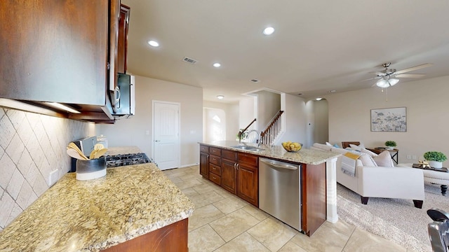 kitchen featuring a center island with sink, dishwasher, ceiling fan, and light stone countertops