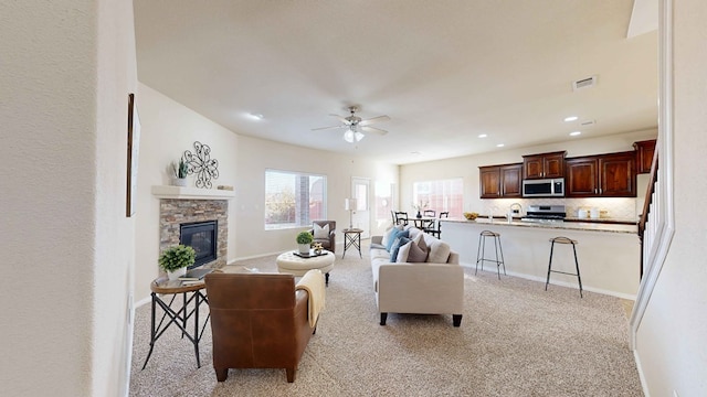 living room with light carpet, a stone fireplace, and ceiling fan