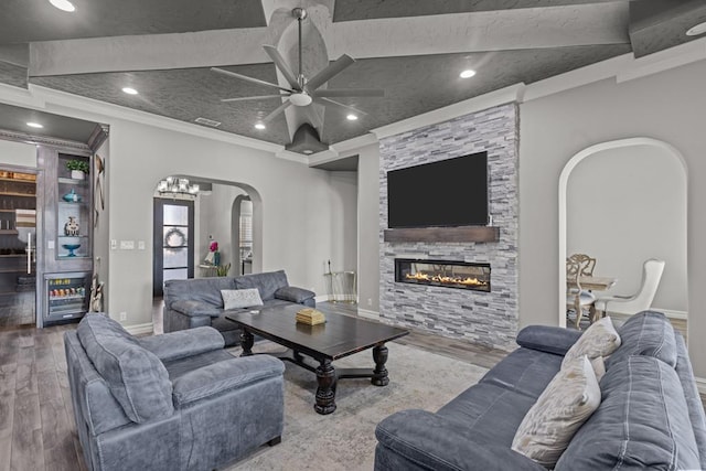 living room with crown molding, a stone fireplace, ceiling fan, and hardwood / wood-style flooring