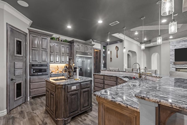 kitchen with a large island with sink, appliances with stainless steel finishes, pendant lighting, and dark brown cabinetry