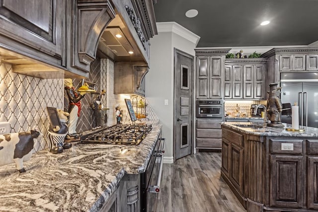 kitchen featuring crown molding, appliances with stainless steel finishes, dark brown cabinets, and dark stone counters