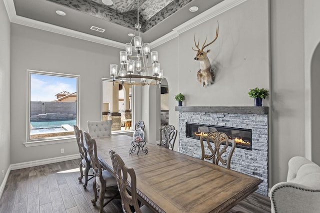 dining area featuring hardwood / wood-style floors, a fireplace, ornamental molding, a raised ceiling, and a chandelier