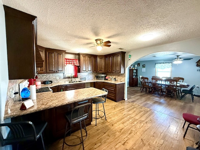 kitchen featuring kitchen peninsula, light wood-type flooring, a breakfast bar, a textured ceiling, and sink