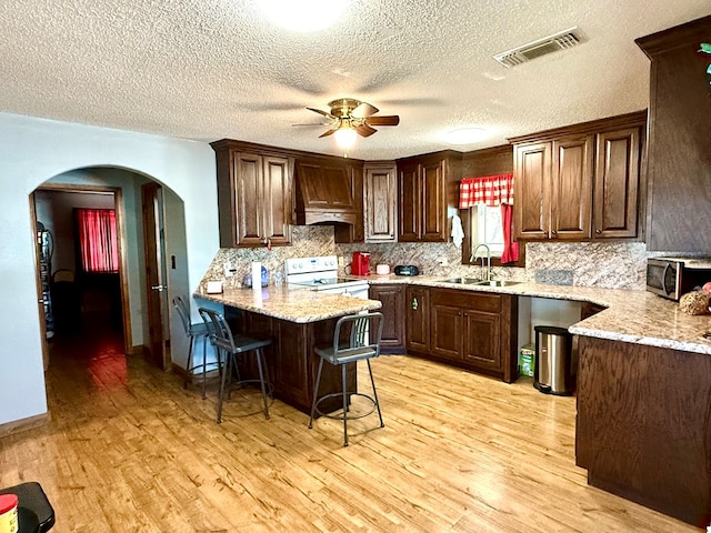 kitchen featuring sink, white electric range oven, premium range hood, kitchen peninsula, and a kitchen bar