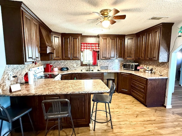 kitchen featuring kitchen peninsula, a breakfast bar, sink, electric range, and light hardwood / wood-style flooring