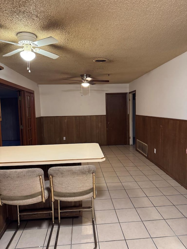 kitchen with wood walls, visible vents, a textured ceiling, and wainscoting