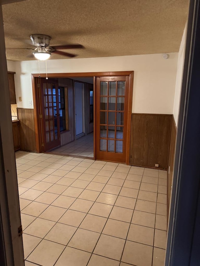 empty room with light tile patterned floors, wooden walls, a textured ceiling, and wainscoting