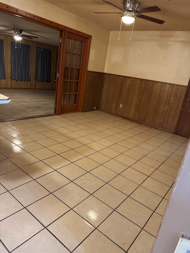 unfurnished room with a textured ceiling, wainscoting, a ceiling fan, and wooden walls