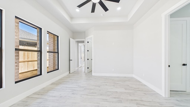 empty room with baseboards, a raised ceiling, ceiling fan, light wood-style floors, and recessed lighting