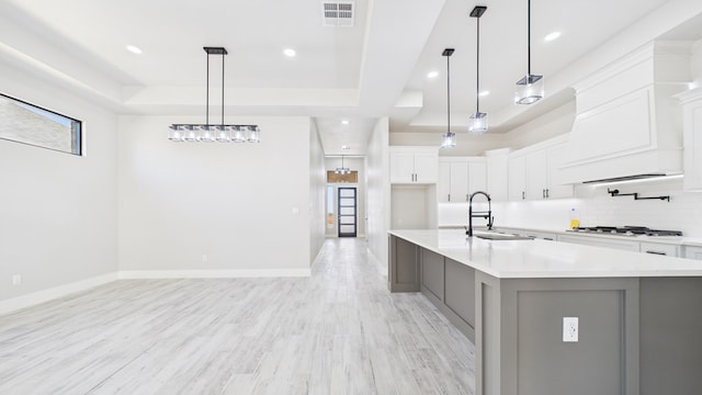 kitchen with a raised ceiling, light countertops, visible vents, backsplash, and a sink