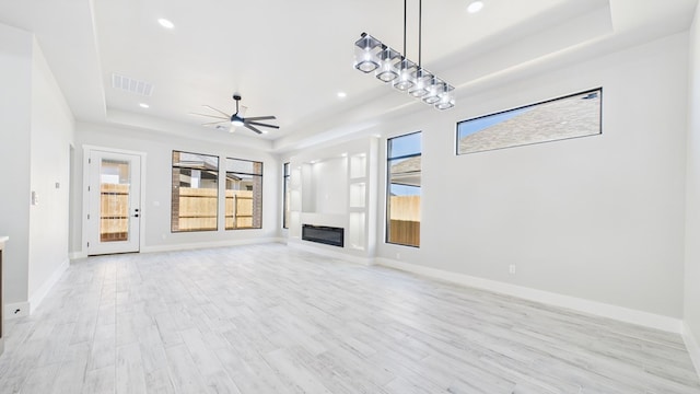 unfurnished living room with a glass covered fireplace, plenty of natural light, a raised ceiling, and visible vents