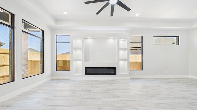 unfurnished living room featuring light wood finished floors, baseboards, a wealth of natural light, and a glass covered fireplace