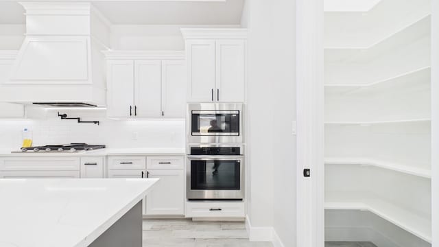 kitchen with light stone counters, premium range hood, white cabinets, appliances with stainless steel finishes, and tasteful backsplash