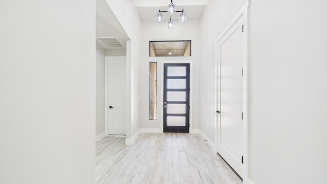 foyer featuring an inviting chandelier, wood finished floors, visible vents, and baseboards