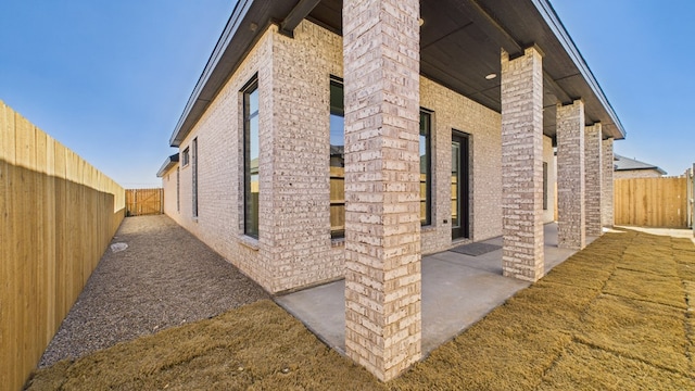 view of side of home featuring a fenced backyard, a patio, and brick siding