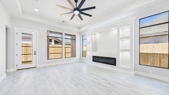 unfurnished living room featuring plenty of natural light, visible vents, wood finished floors, and a glass covered fireplace