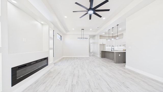 unfurnished living room with light wood-type flooring, baseboards, a raised ceiling, and a glass covered fireplace