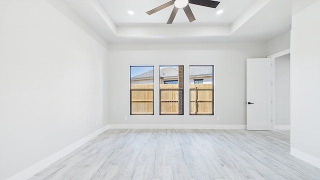 empty room featuring ceiling fan, light wood-style flooring, recessed lighting, baseboards, and a raised ceiling