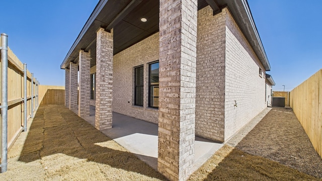 view of side of property featuring brick siding, a patio, a fenced backyard, and central air condition unit