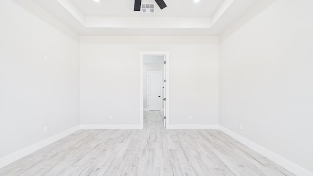 unfurnished room with visible vents, baseboards, a ceiling fan, light wood-style flooring, and a tray ceiling