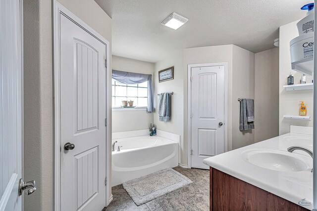 bathroom with a textured ceiling, vanity, and a tub