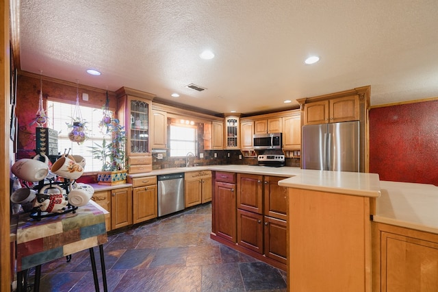 kitchen featuring stainless steel appliances, brown cabinets, light countertops, and glass insert cabinets