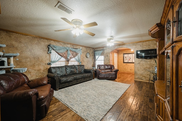 living room featuring dark wood-style floors, arched walkways, visible vents, ornamental molding, and a textured ceiling