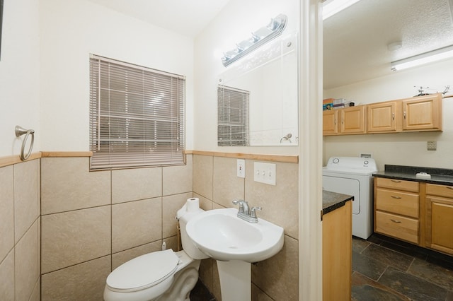 half bathroom featuring tile walls, washer / clothes dryer, toilet, stone finish floor, and a sink