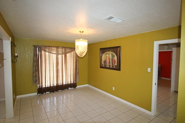 spare room with light tile patterned flooring, a textured ceiling, and an inviting chandelier