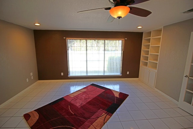 tiled empty room featuring ceiling fan, built in features, and a textured ceiling