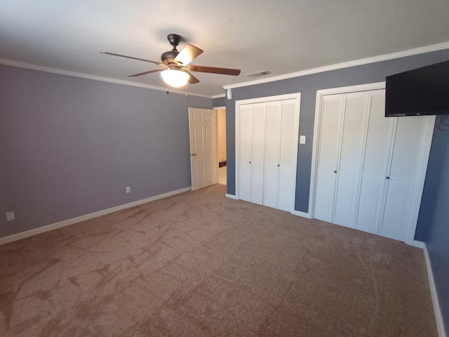 unfurnished bedroom featuring multiple closets, carpet floors, ceiling fan, and crown molding