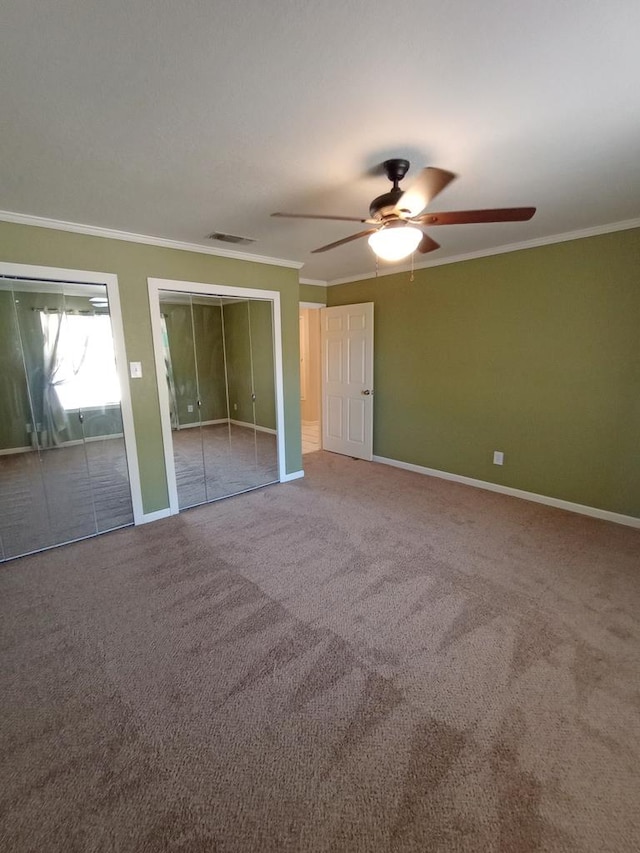 unfurnished bedroom with carpet flooring, ceiling fan, crown molding, and two closets