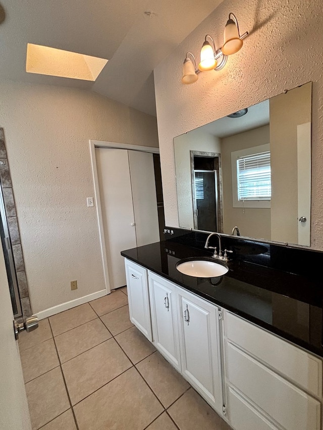 bathroom with tile patterned floors, vanity, and lofted ceiling with skylight