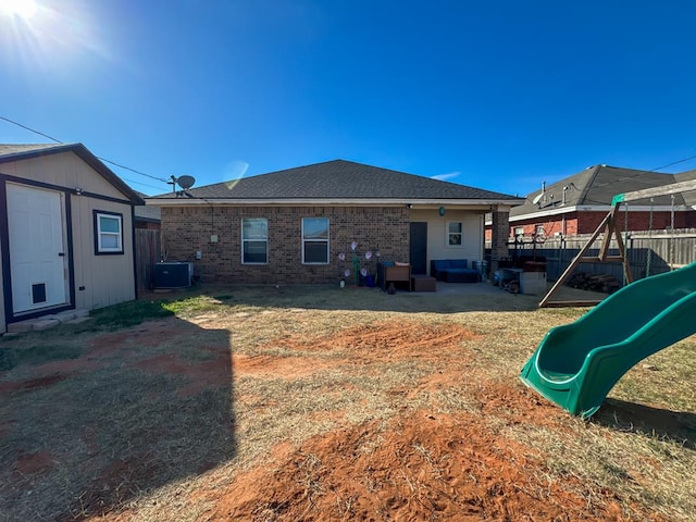 rear view of property featuring a playground, cooling unit, and a shed