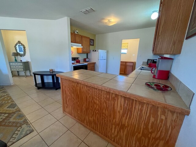 kitchen with sink, black electric range oven, white refrigerator, tile countertops, and light tile patterned flooring