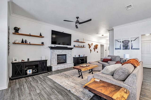 living area with visible vents, a brick fireplace, ornamental molding, wood finished floors, and a ceiling fan