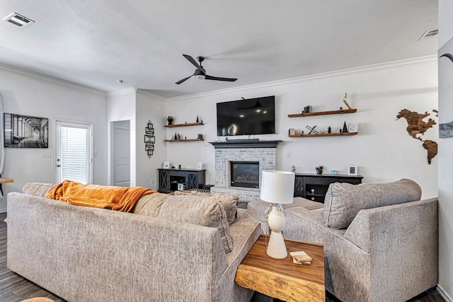 living area featuring visible vents, a brick fireplace, crown molding, wood finished floors, and a ceiling fan