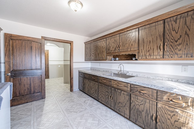 kitchen featuring light stone countertops, dark brown cabinets, and sink