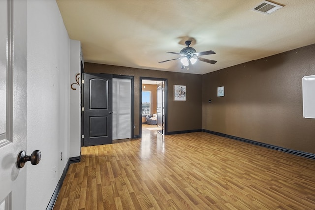 empty room with ceiling fan, light wood-type flooring, and a textured ceiling