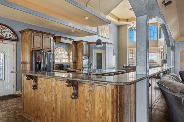 kitchen featuring a towering ceiling, dark stone counters, pendant lighting, a chandelier, and appliances with stainless steel finishes