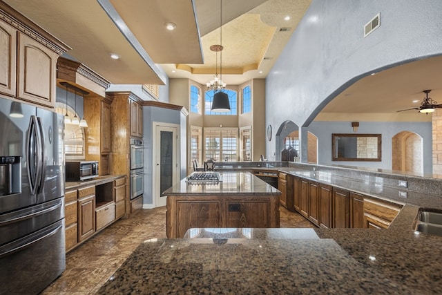 kitchen featuring kitchen peninsula, appliances with stainless steel finishes, a raised ceiling, a center island, and hanging light fixtures