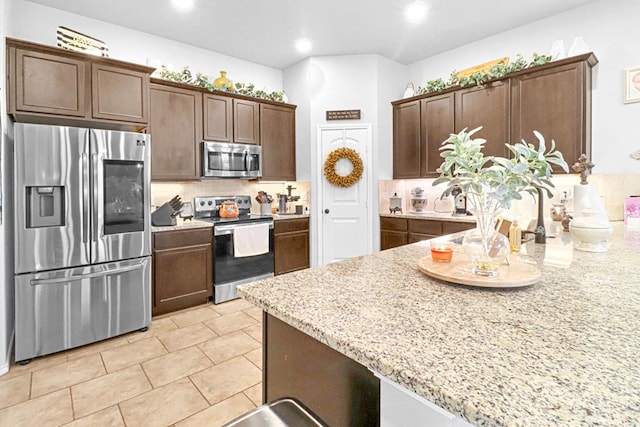 kitchen featuring light stone countertops, decorative backsplash, dark brown cabinetry, and stainless steel appliances