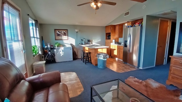 kitchen featuring lofted ceiling, ceiling fan, stainless steel fridge, a kitchen island, and a kitchen bar