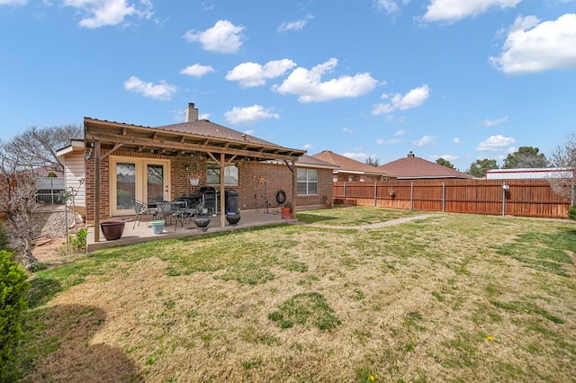 rear view of property featuring brick siding, a lawn, a patio, and a fenced backyard