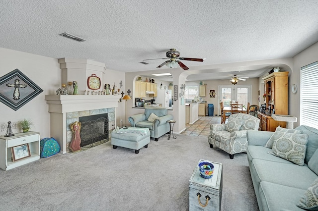 living room with visible vents, ceiling fan, a tile fireplace, a textured ceiling, and light colored carpet